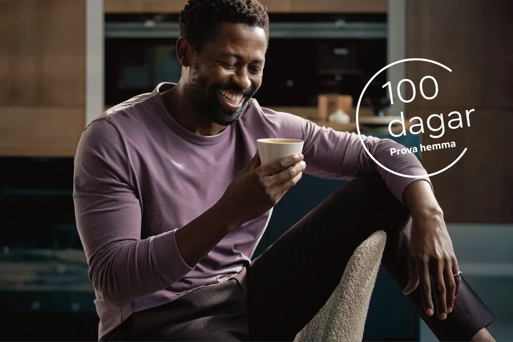 Leende man i lila skjorta håller kaffemugg, "100 dagar" textöverlägg.