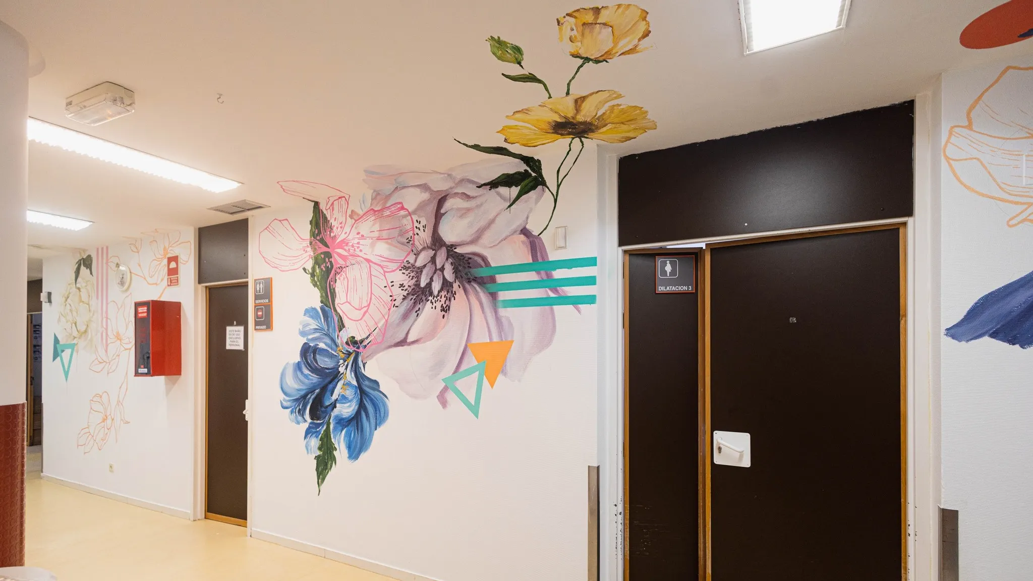 Mural floral colorido que decora un pasillo con puertas y una lámpara de techo. 