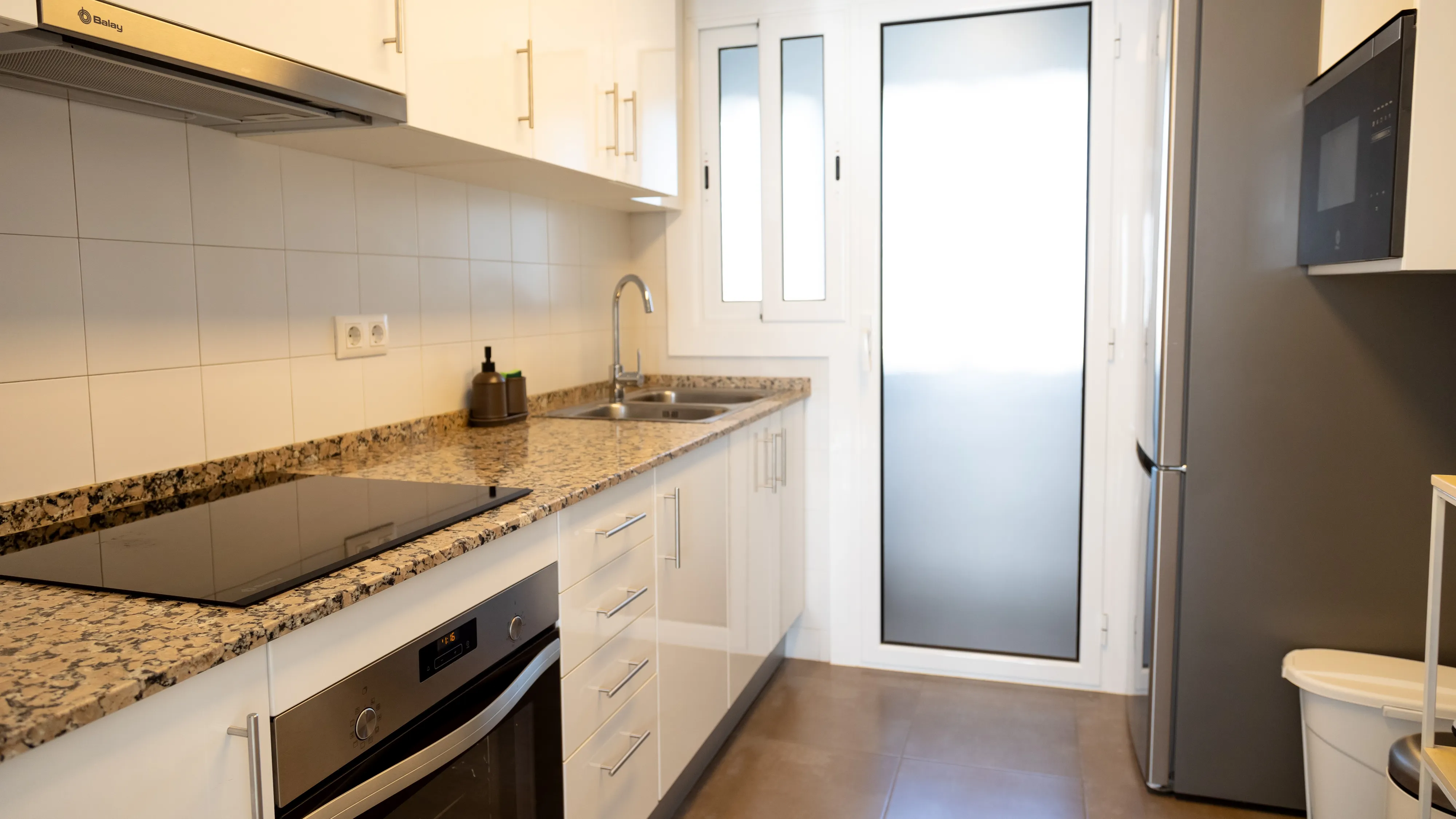 Cocina de hogar con muebles blancos, encimeras de granito y electrodomésticos de acero inoxidable. 