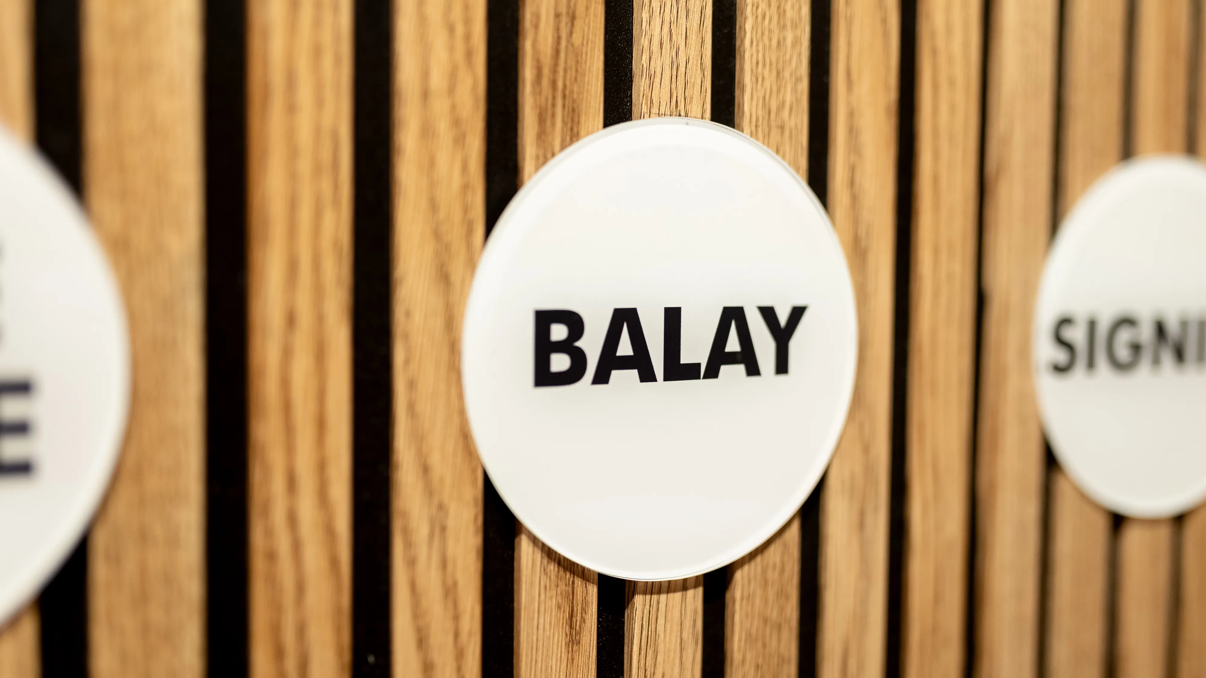 Listones de madera con cartel circular de color blanco donde aparece la palabra "BALAY". 