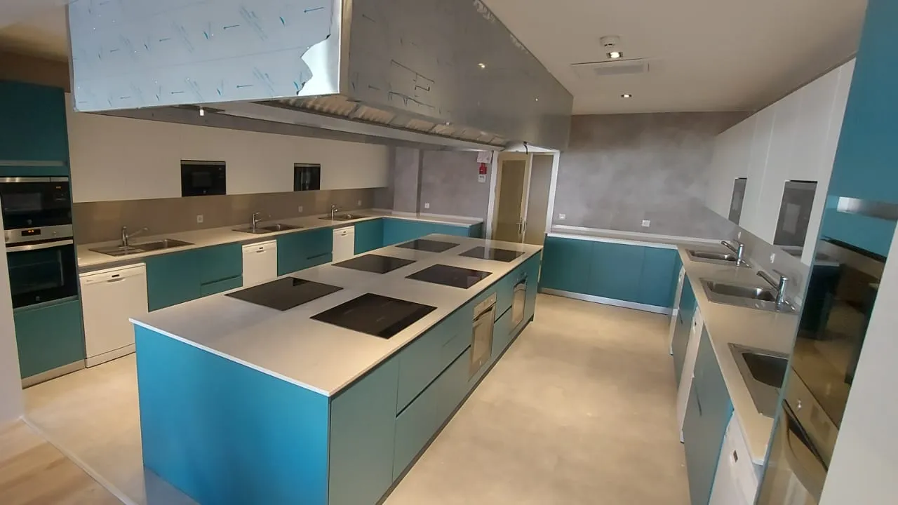 Cocina oomunitaria con numerosos electrodomésticos en acero inoxidabley fregaderos en una gran isla central. 