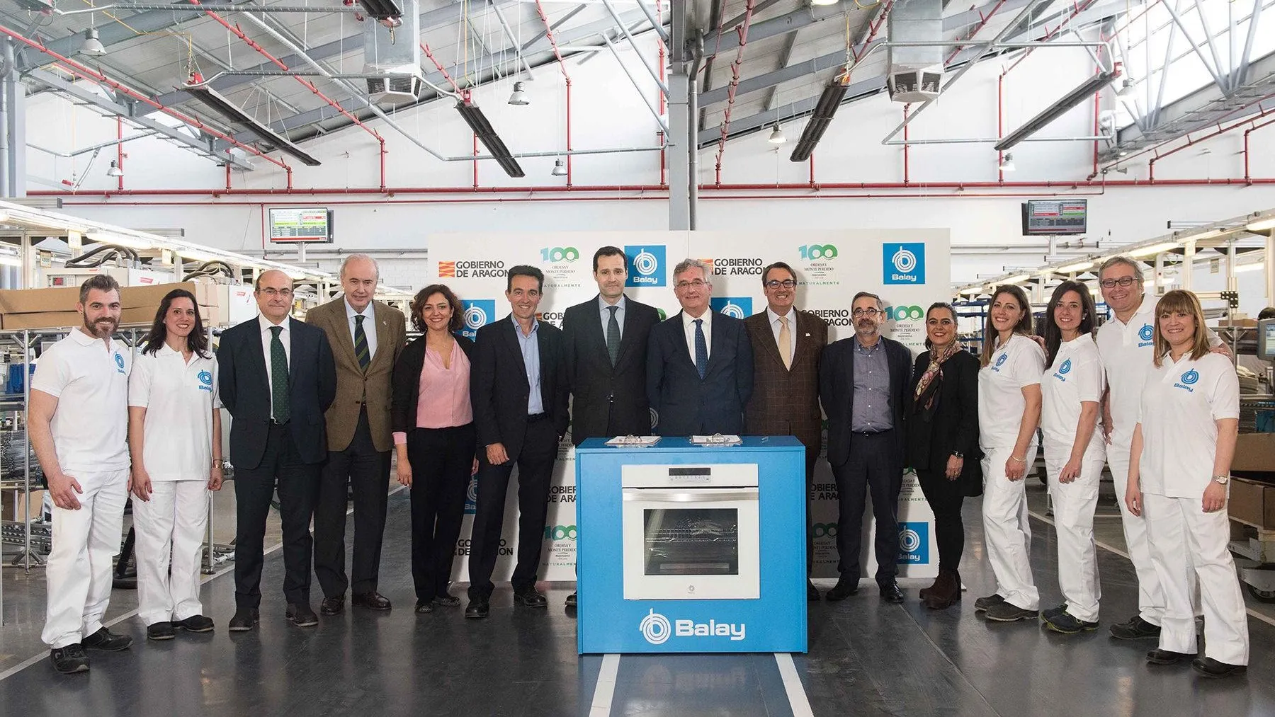 Grupo de profesionales de negocios posando frente a la exhibición de electrodomésticos Balay en un entorno industrial. 