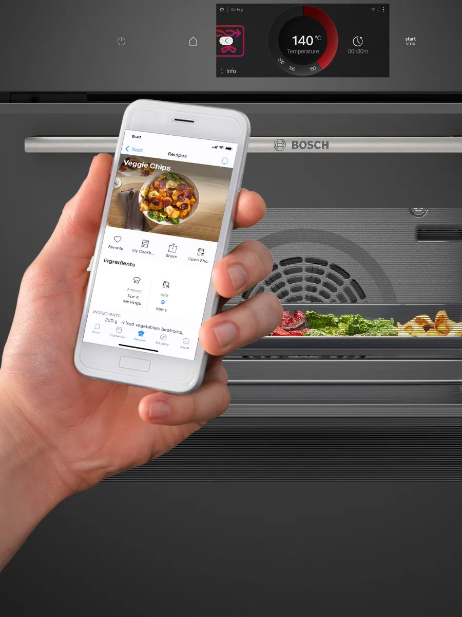 Mano che tiene uno smartphone con app di ricette, accanto a un forno Bosch con display digitale. 