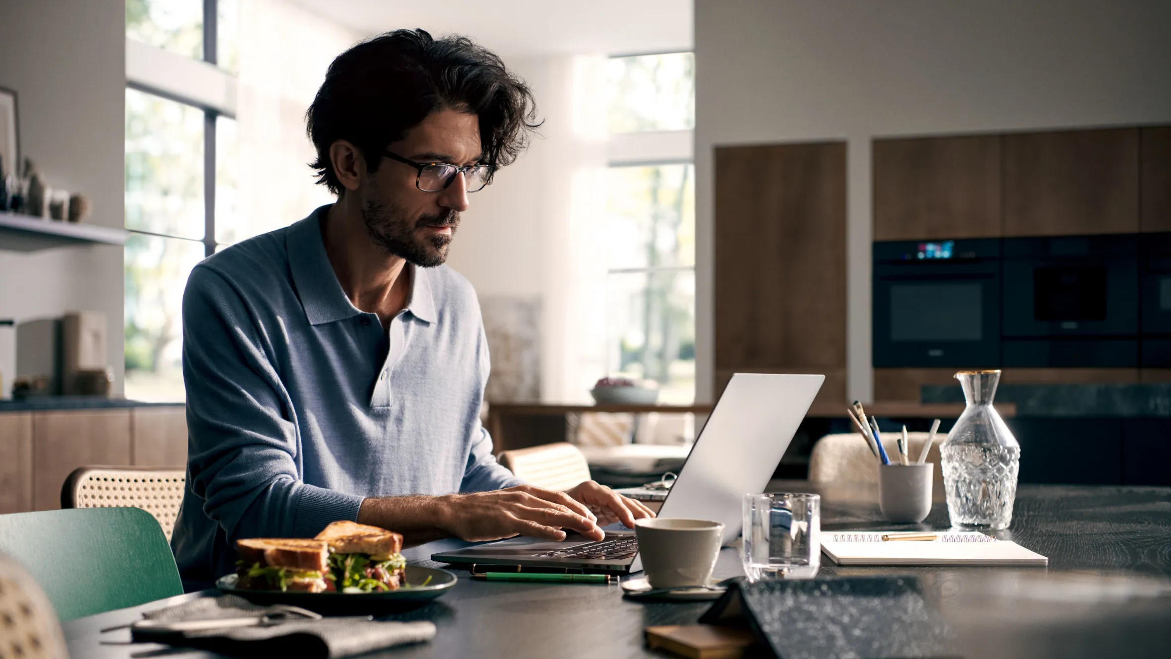 Der Mann arbeitet an Laptop, während er Sandwich in der modernen Küche isst.