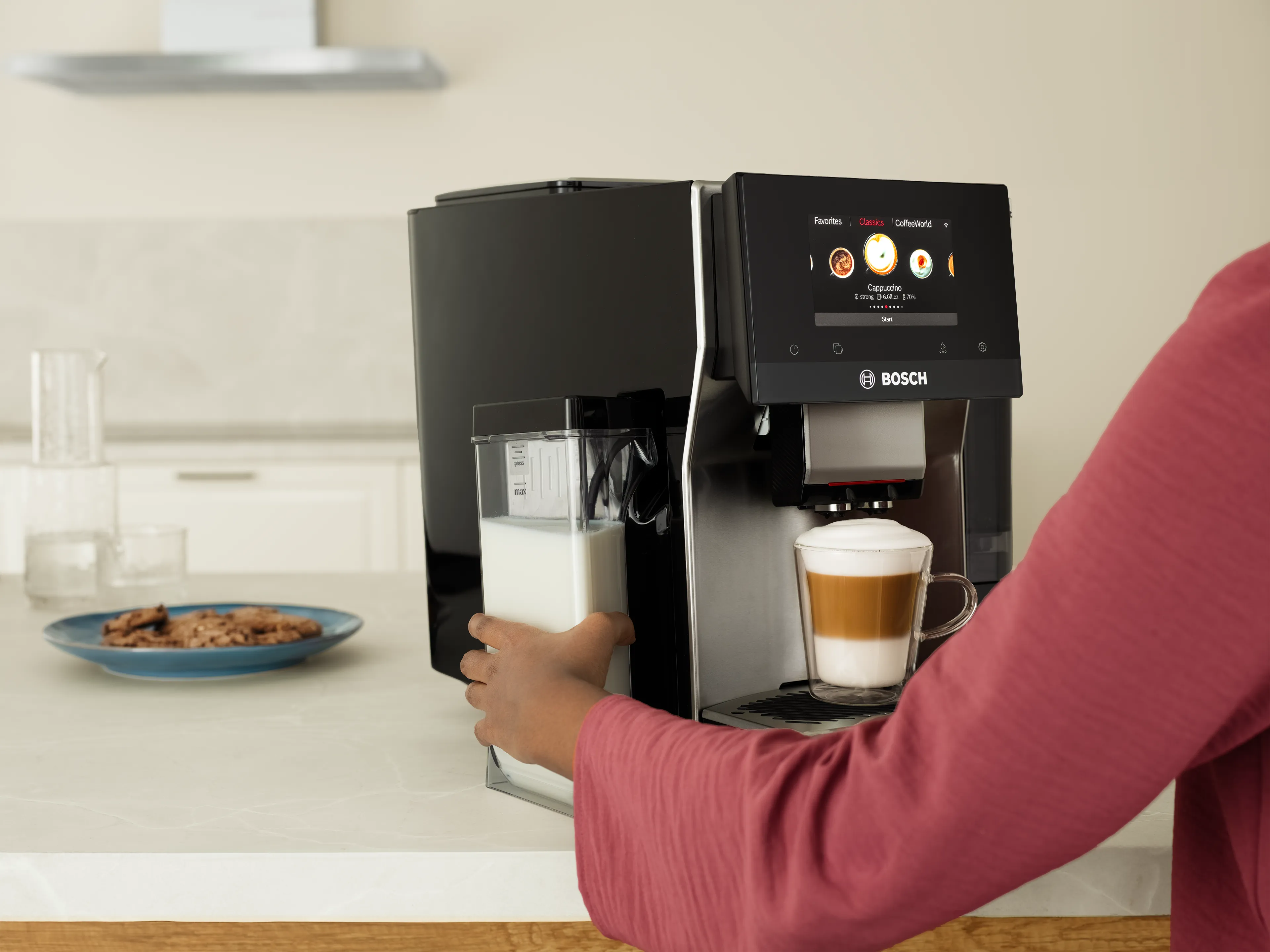Person using a Bosch coffee machine to make a cappuccino in a modern kitchen.