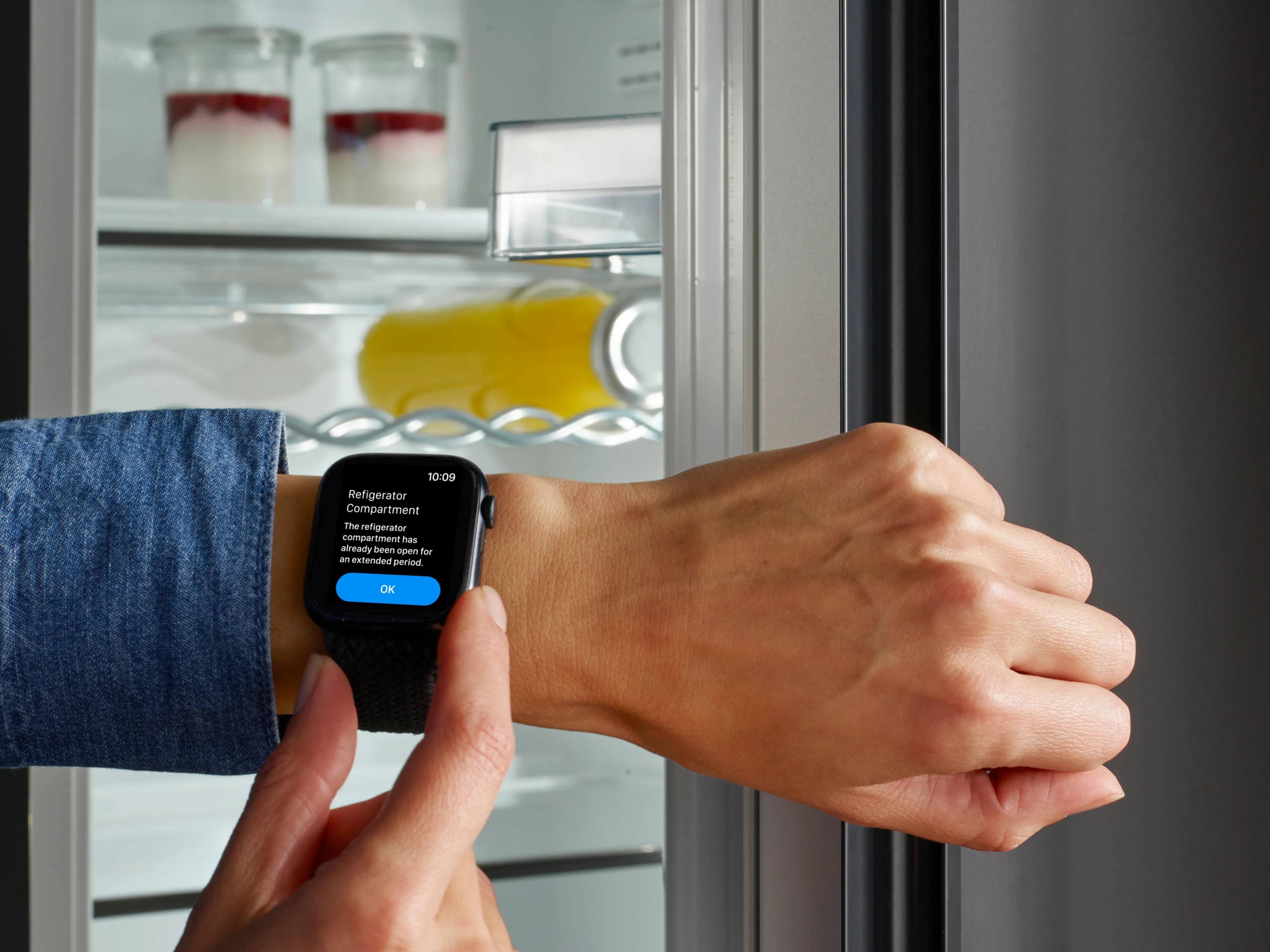Persona con uno smartwatch che riceve una notifica di avviso per il vano frigorifero rimasto aperto troppo a lungo.