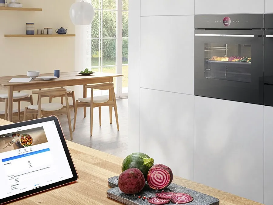 Cocina moderna con mesa de madera, sillas, horno y receta de visualización de tabletas.