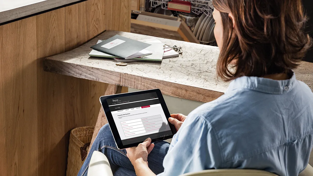 Vrouw die aan een tablet werkt aan een houten bureau met boeken en papieren.