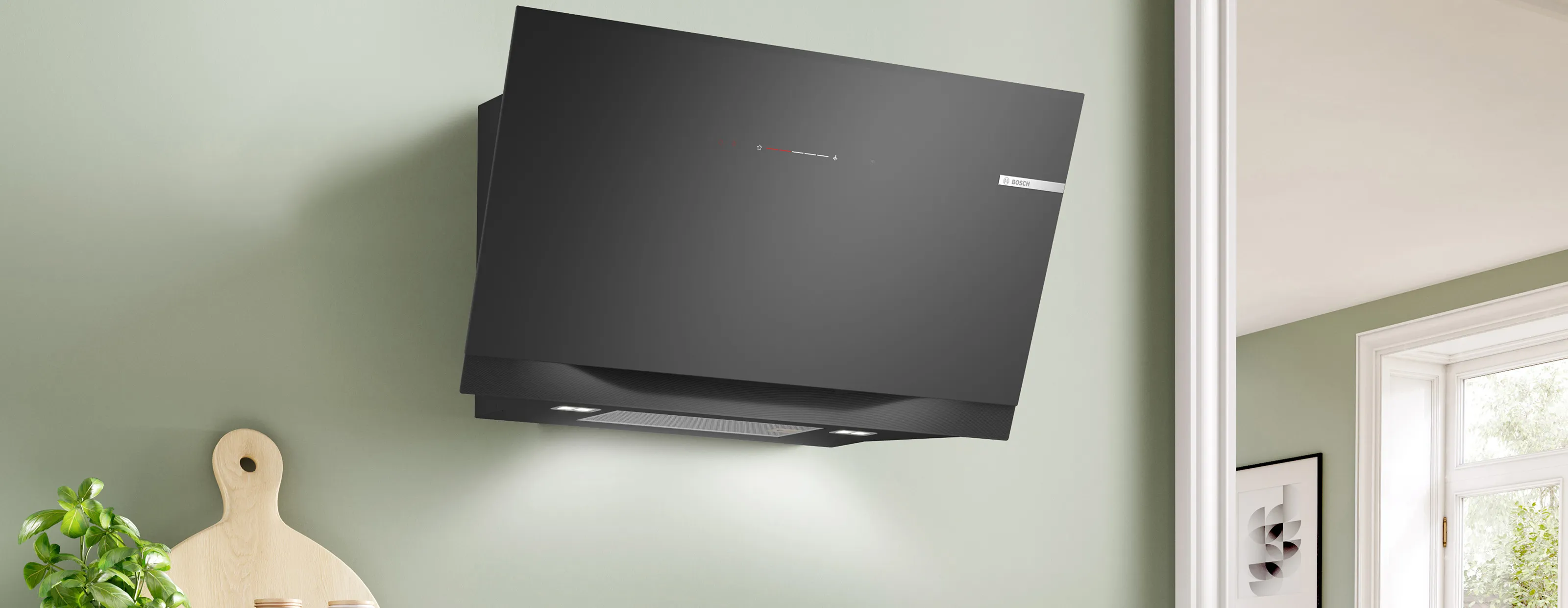 A black and steel wall-mounted, inclined hood in a modern kitchen with green walls.