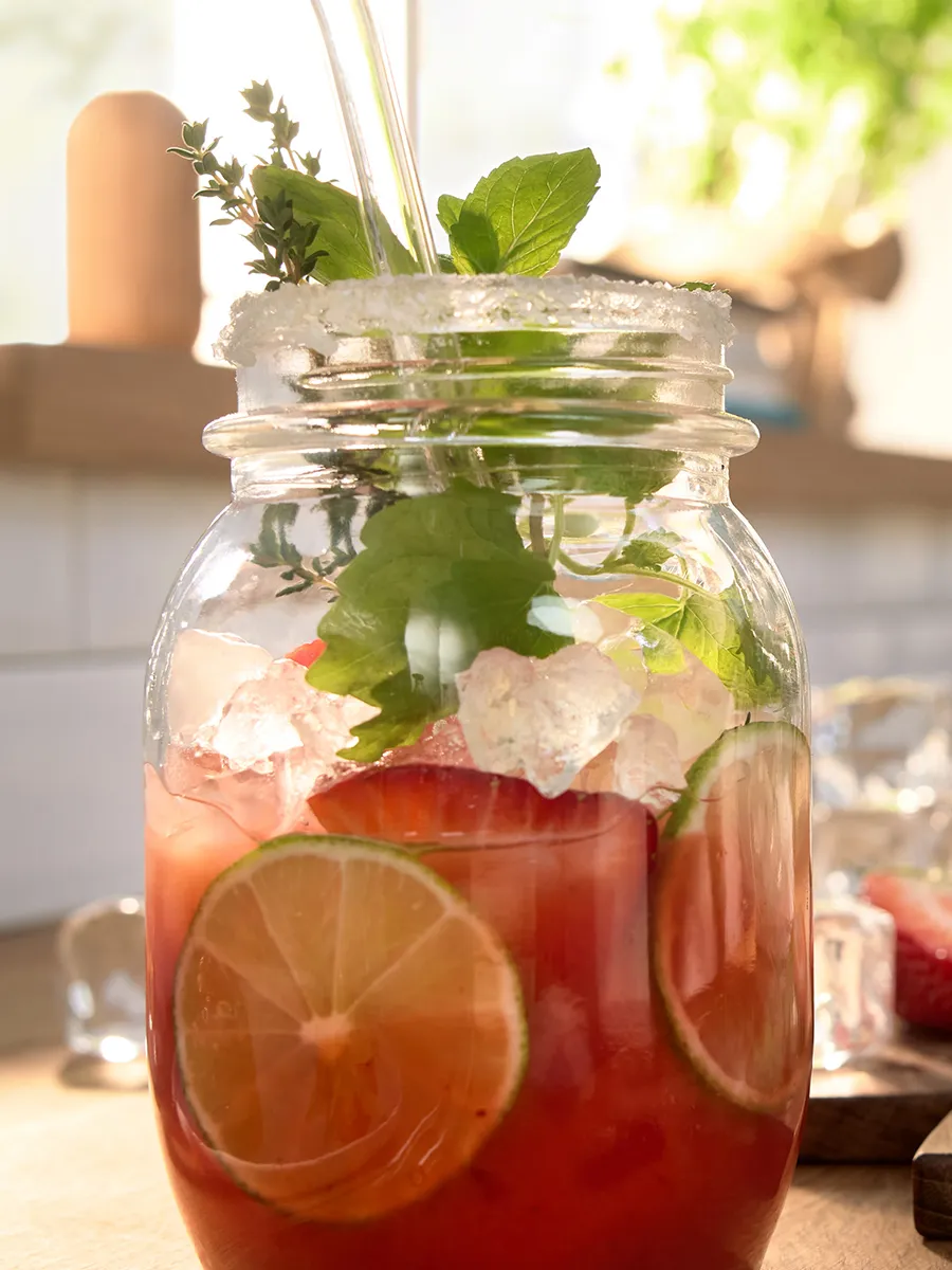 Sap gemaakt met een citruspers in een glazen pot met ijsklontjes en verse fruitplakken op het keukentop.