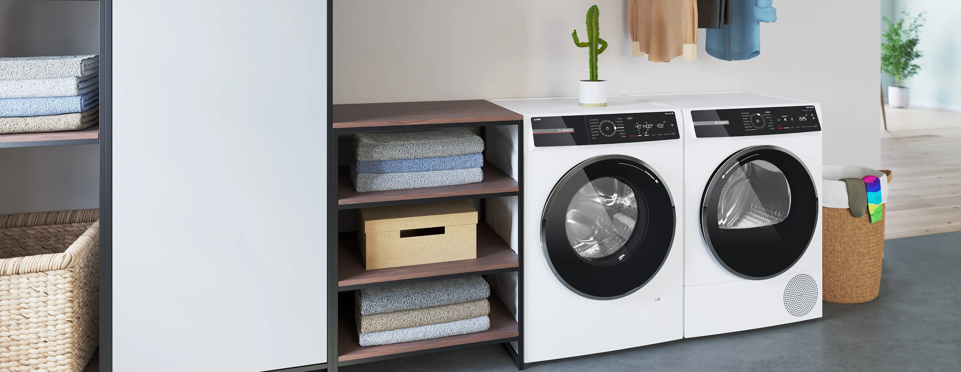 Eine weiße Bosch-Waschmaschine und ein passender Wäschetrockner stehen nebeneinander in einem modern eingerichteten Hauswirtschaftsraum neben einem Holzregal mit Handtüchern.