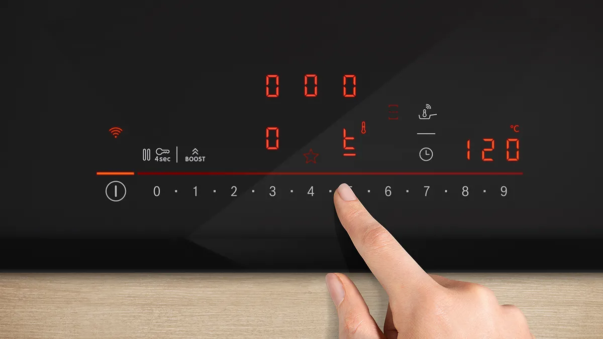 Finger adjustment of a digital control panel with red LED indicators and touch buttons on a sleek black appliance.