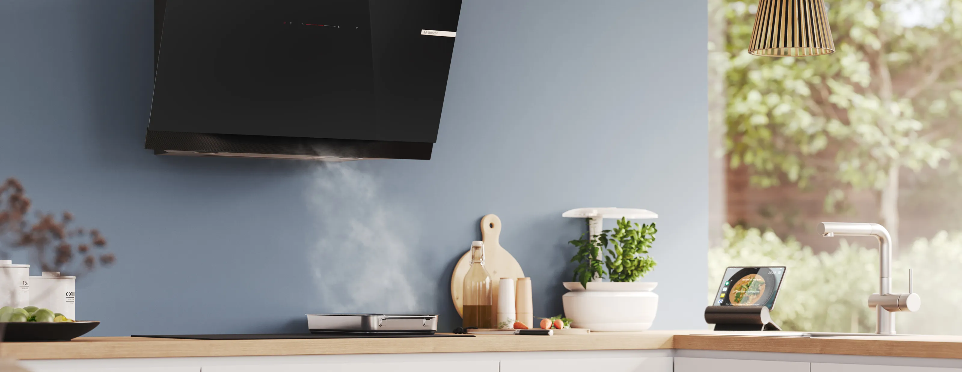 A Bosch black angled cooker hood extracting steam from a pan in a modern kitchen with a smart herb garden.