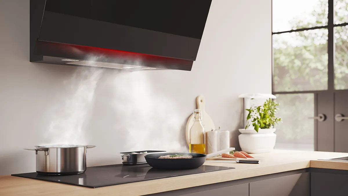 A Bosch black angled extractor hood with red ambient lighting extracting steam from cooking pans in a modern kitchen.
