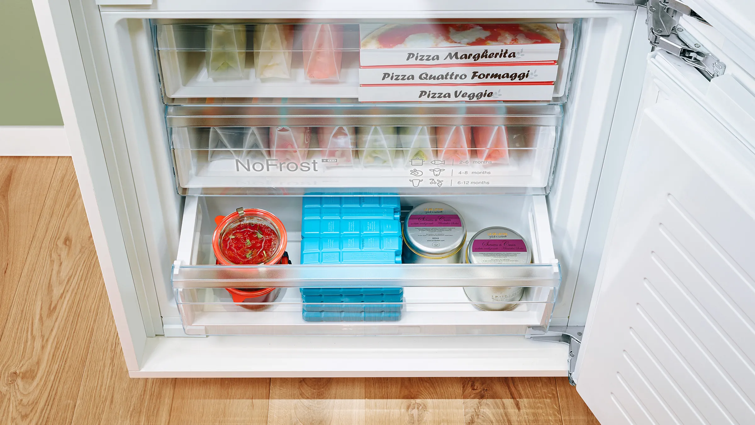 Inside of a freezer with labeled frozen pizzas, an ice tray, and containers of frozen food.
