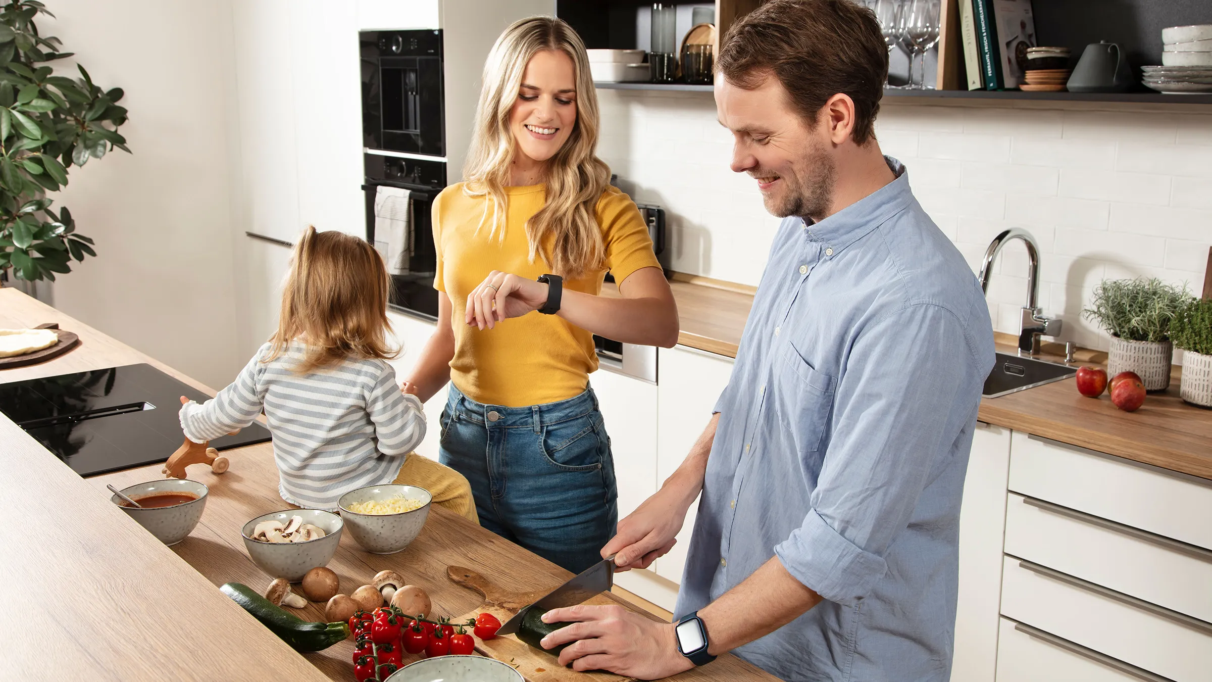 Family preparing a meal together in a modern kitchen with fresh vegetables and ingredients on the counter.