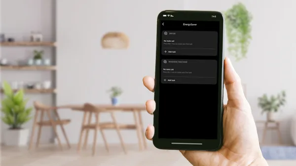 Een persoon die een smartphone vasthoudt met een interface van de 'EnergySaver' app, tegen een moderne, heldere woonkamer als achtergrond.