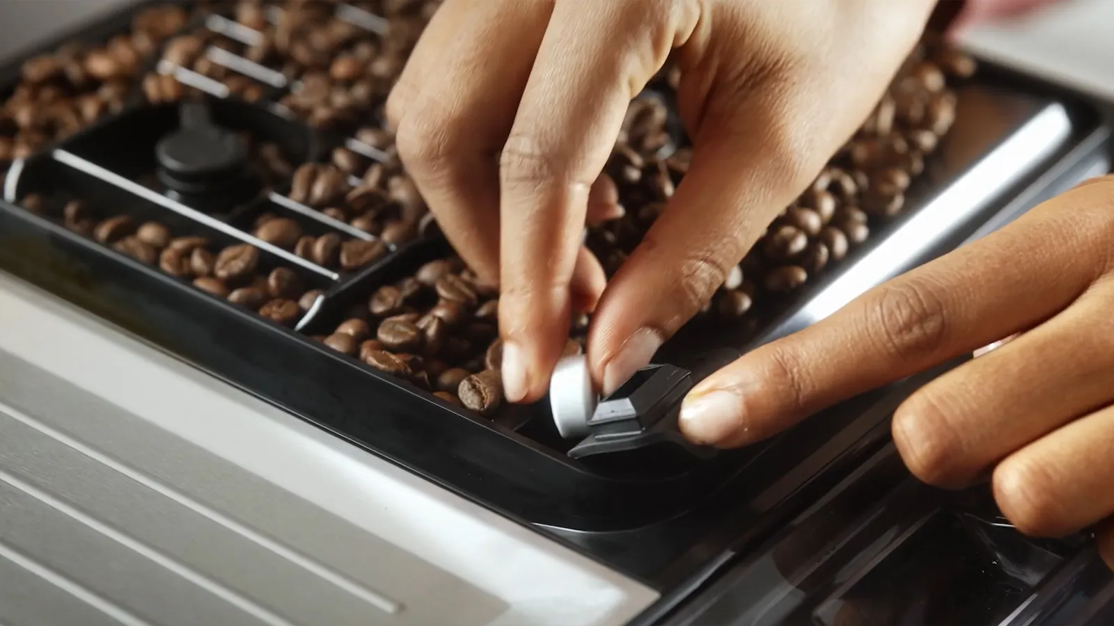Hand adjusting a setting on a  Boschcoffee machine with coffee beans visible in the tray.