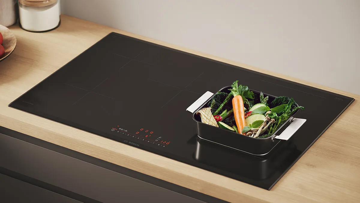 A large induction hob with a frying pan cooking a steak.