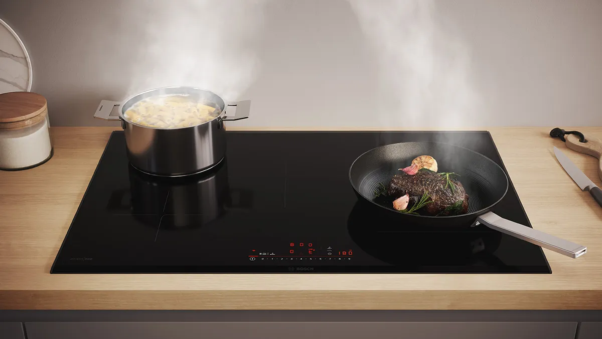 Induction cooktop with cooking pots, one containing steaming food, on a wooden kitchen counter.