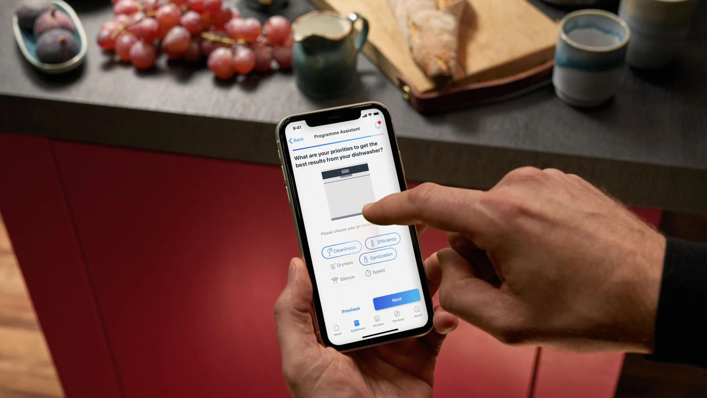 Person mit Smartphone auf Online-Banking-App auf Küchentheke mit Trauben und Brot zugreifen.