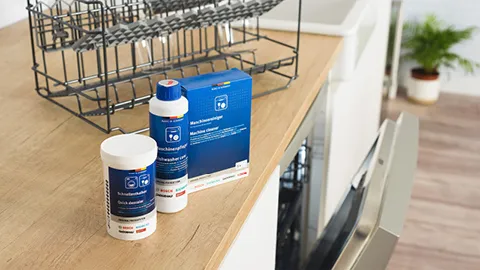 Bosch Dishwasher cleaning products on a wooden countertop next to an open dishwasher door.