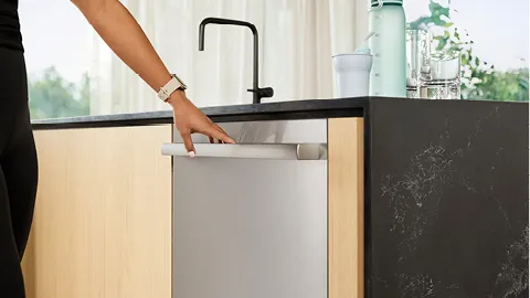 Person opening a Bosch stainless steel dishwasher integrated into a modern kitchen counter.