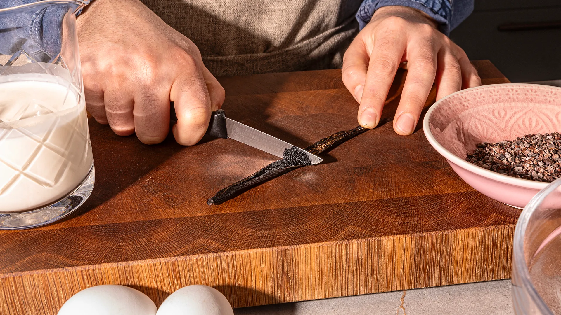 Hands chopping ingredients on a wooden cutting board, including eggs and spices, for cooking or baking.