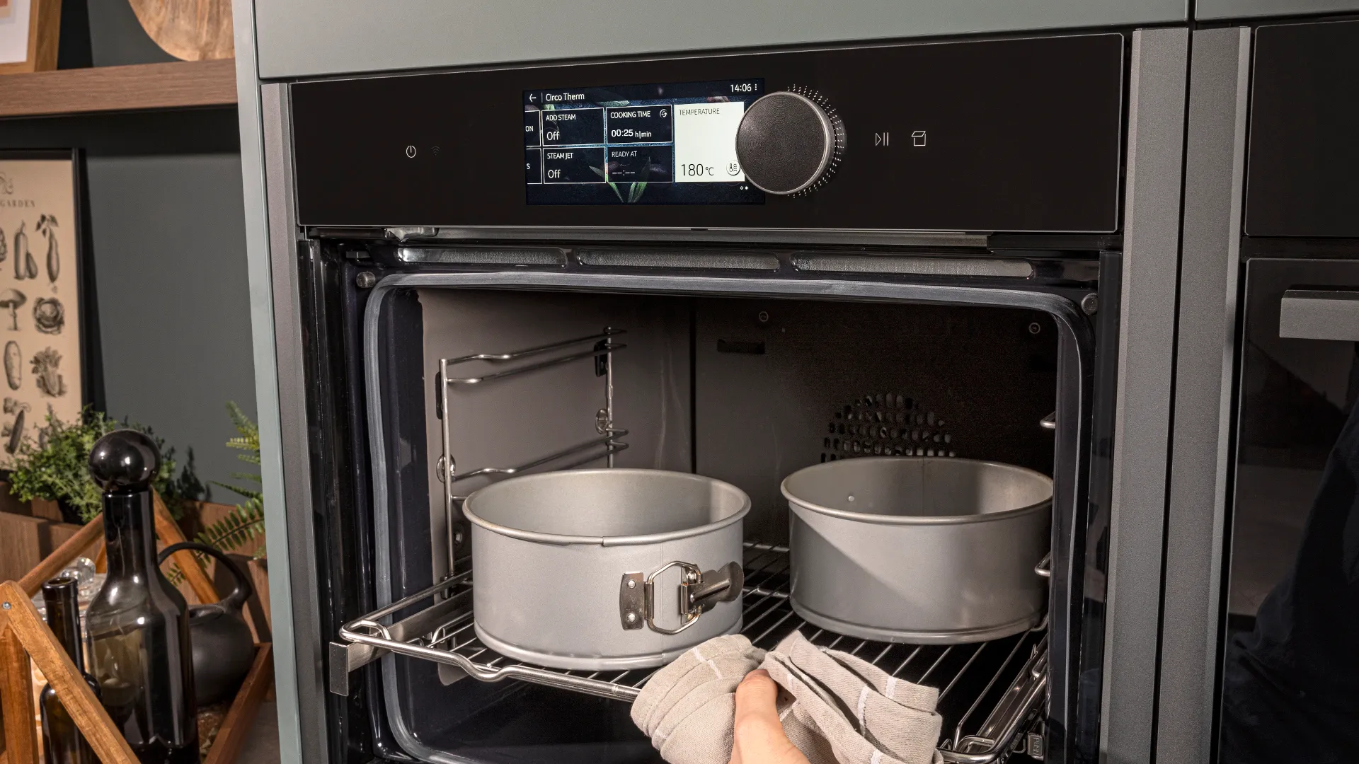 Oven interior with baking dishes, kitchen utensils, and a hand visible adjusting the oven controls.