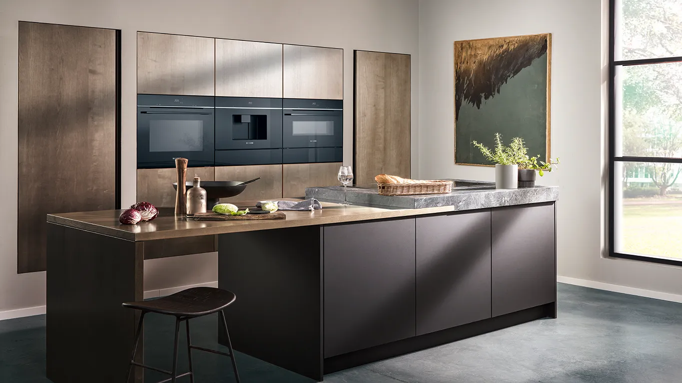 מטבח מודרני עם אי כהה, מכשירי חשמל אלגנטיים ואור טבעי, הכולל תוצרת טרייה וצמחים דקורטיביים.