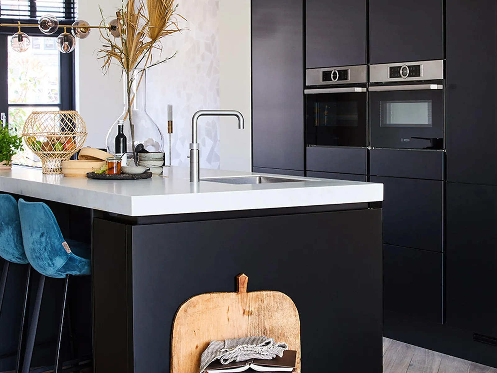 Cuisine moderne avec armoires noires, comptoir blanc, planche à découper en bois et éléments décoratifs.