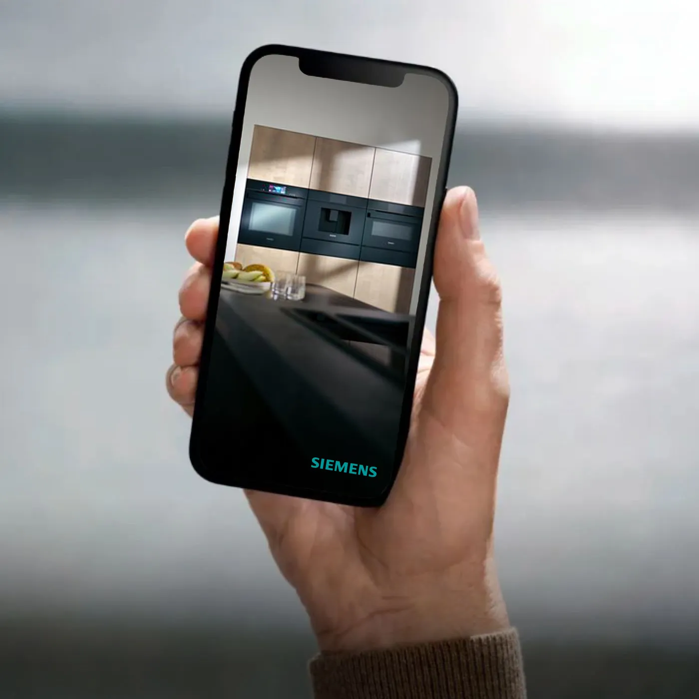 En person holder en smarttelefon som viser en guide til kjøkkenplanlegging med innebygde hvitevarer.