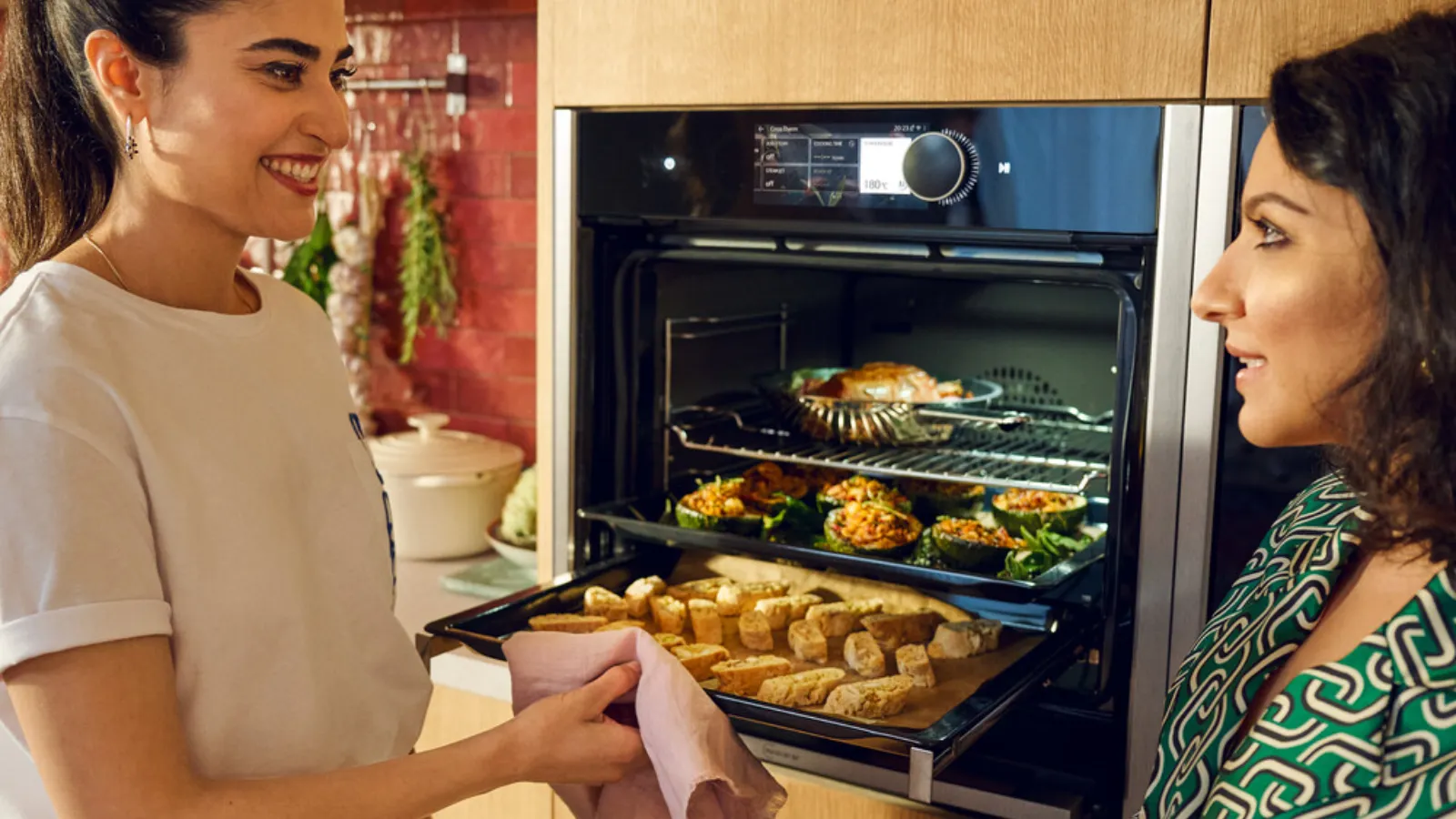 Two women standing in front of an oven with food in it.