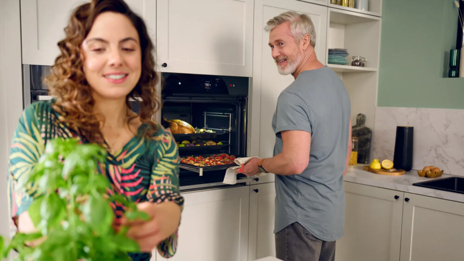 A couple standing in front of an oven, possibly cooking or baking together.