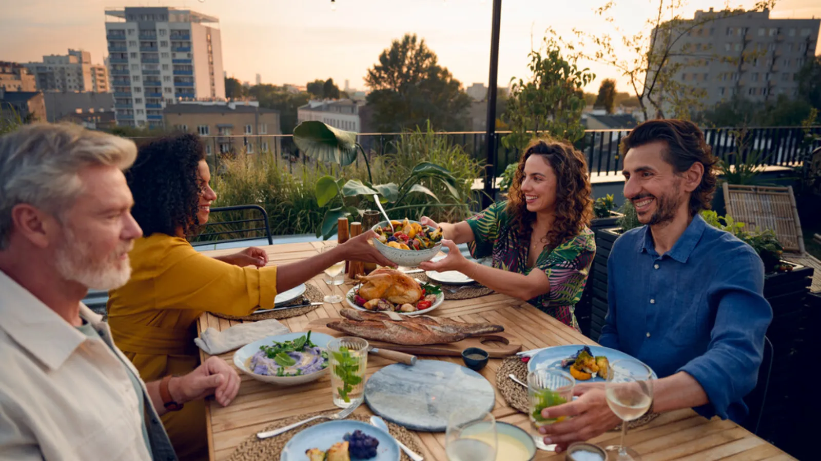 A diverse group of friends laughing and eating together at a picnic table in a sunny park.