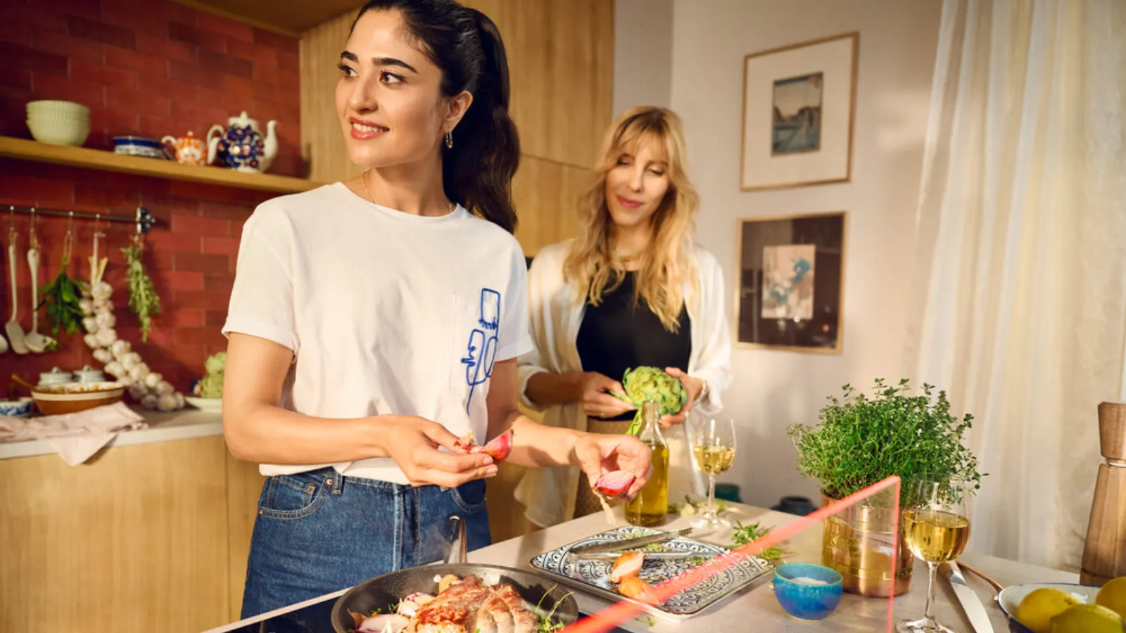 Two women cooking together in a kitchen, chopping vegetables and stirring pots.