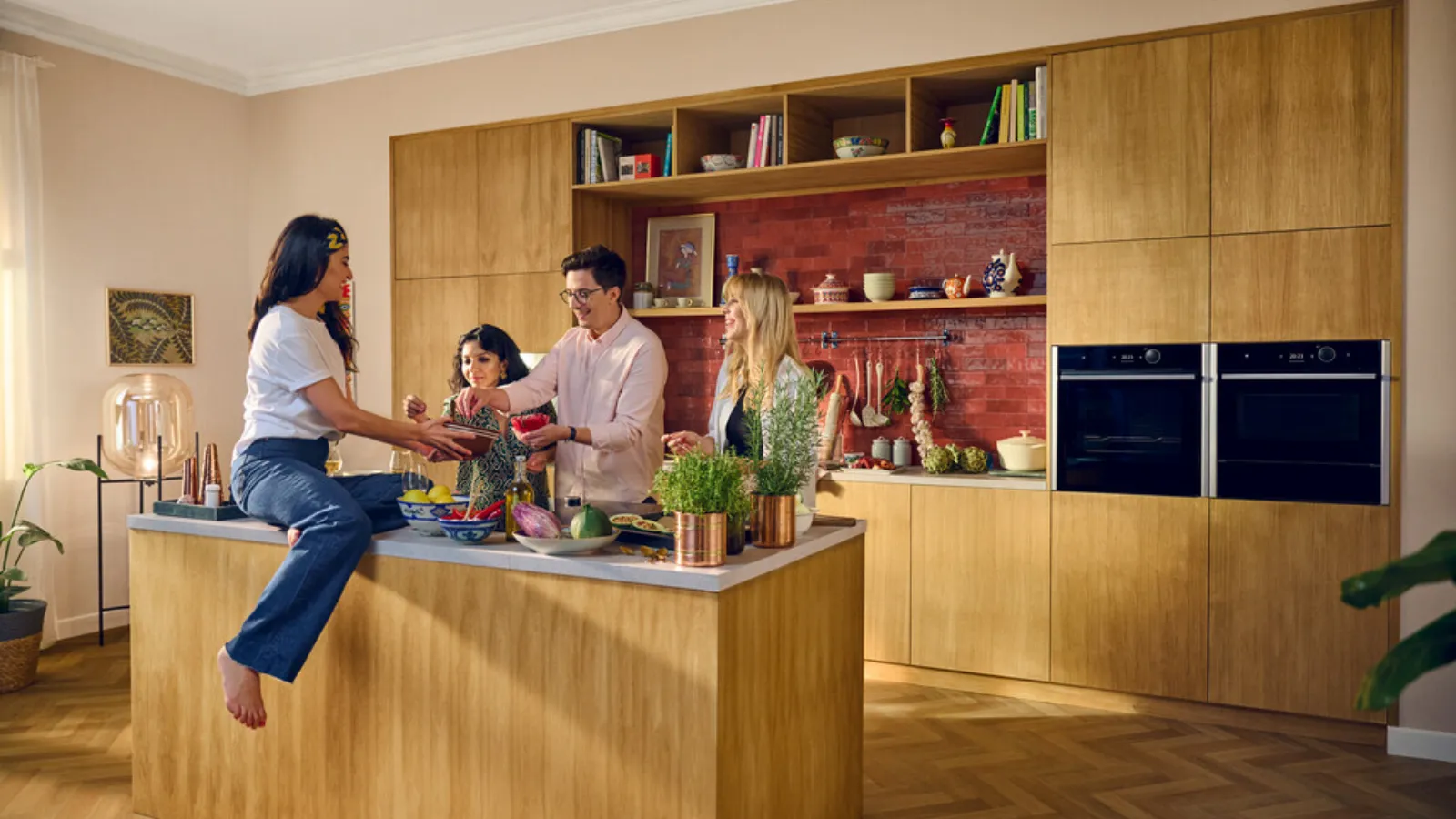 A family of four standing around a kitchen island, smiling and talking while preparing a meal together.