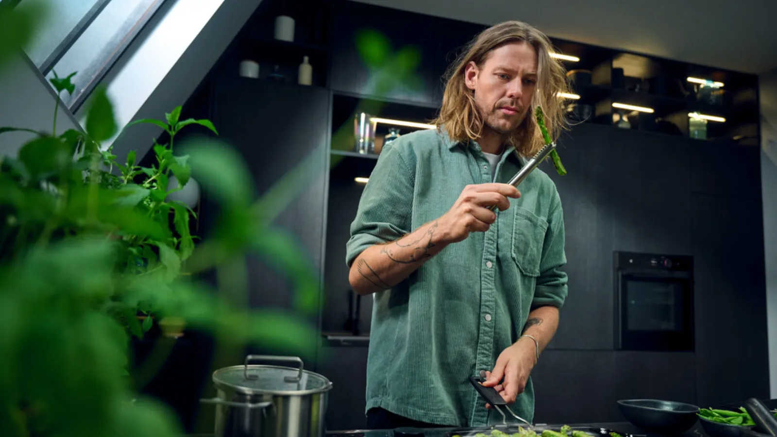  A man with long hair preparing a meal in a kitchen, stirring a pot on the stove