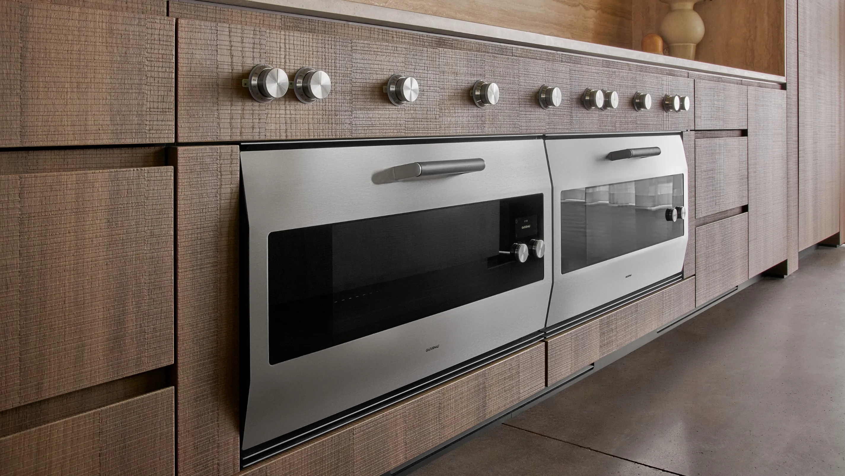 Two Gaggenau EB 333 ovens displayed in the Houston Flagship showroom, surrounded by textured plaster and natural wood
