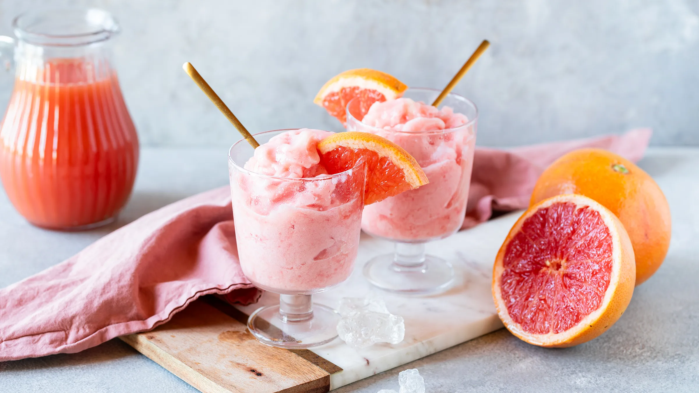 Două pahare de granita cremoasă de grepfrut pe o masă din lemn de culoare închisă, decorate cu câte o felie de grepfrut proaspăt.