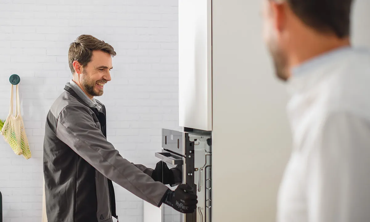 A technician is installing a panel on a white wall-mounted appliance in a modern kitchen.
