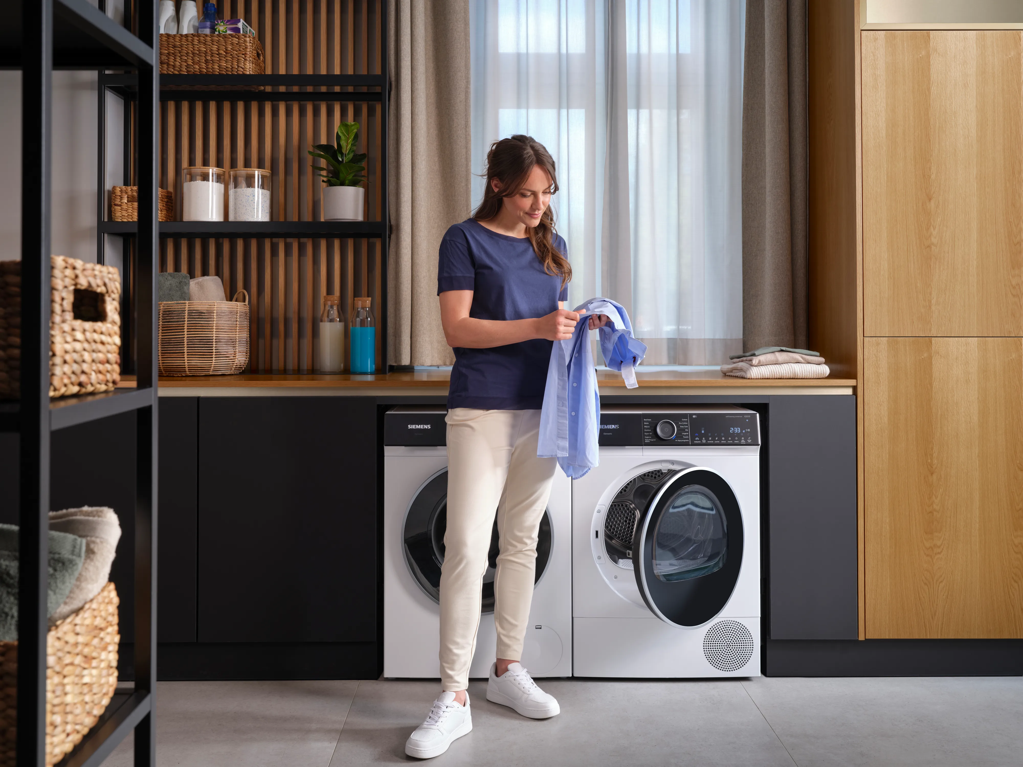 Vrouw met overhemd in handen voor wasmachine en droger in een stijlvolle wasruimte.