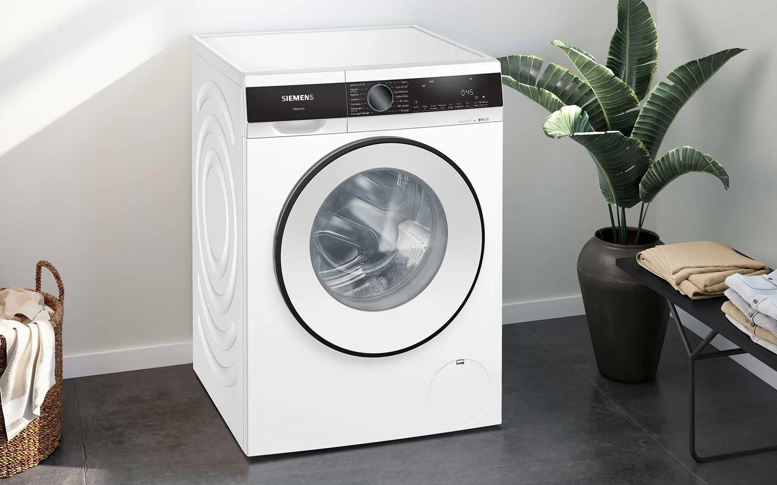 Une machine à laver Siemens moderne dans un intérieur élégant, accompagnée d'une plante en pot et de serviettes.