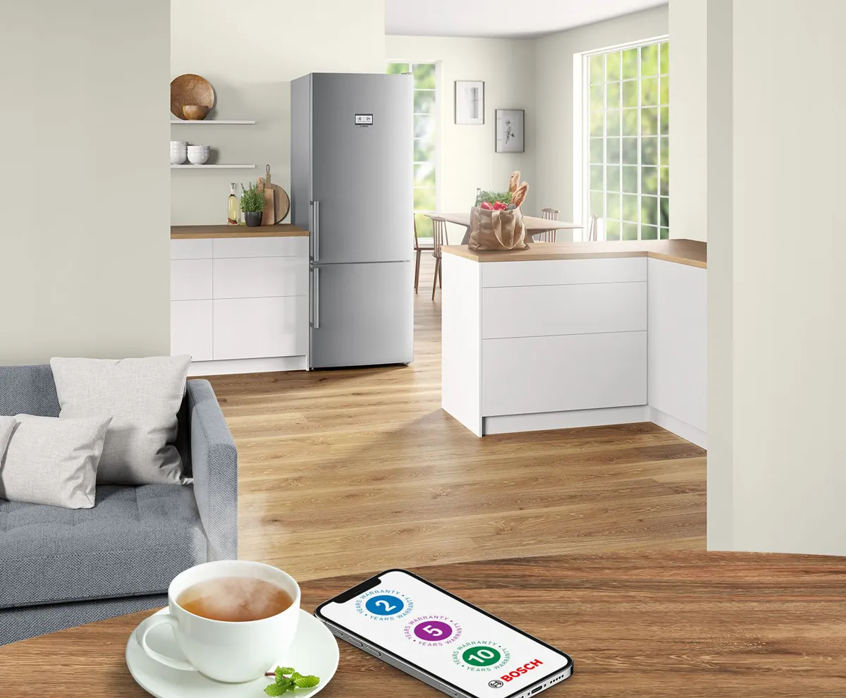 Diverse electrocasnice Bosch intr-o bucatarie moderna. In prim plan telefon mobil care afiseaza extragarantii ale produselor Bosch.