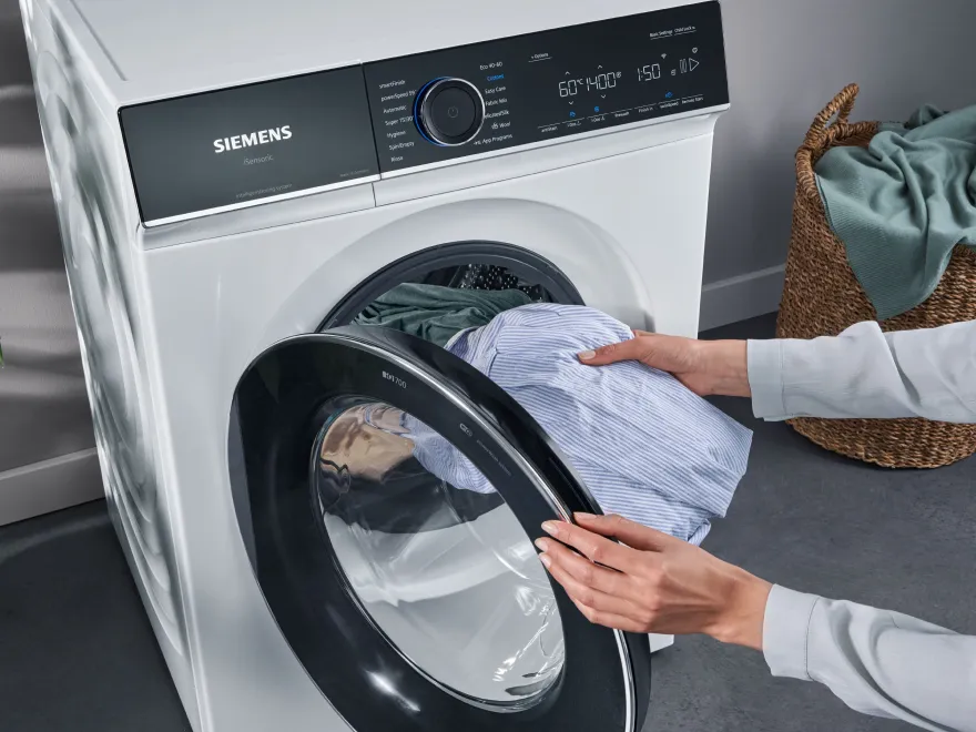 Person loading clothes into a front-loading washing machine.