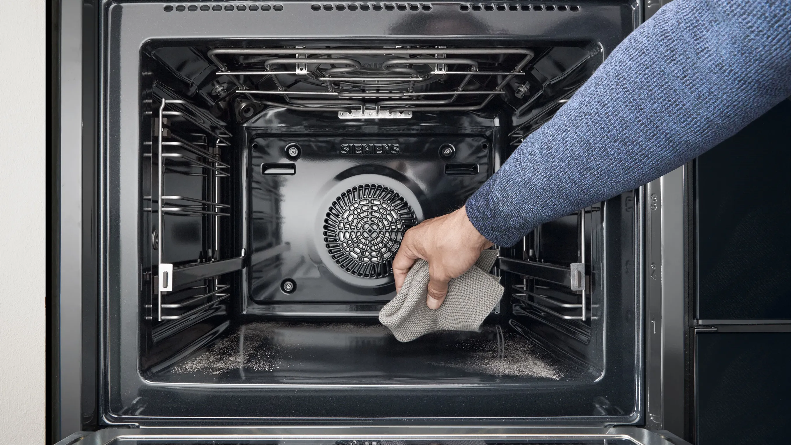 A person easily wipes away the residue from the bottom of a Siemens oven with a cloth, demonstrating the activeClean self-cleaning feature.