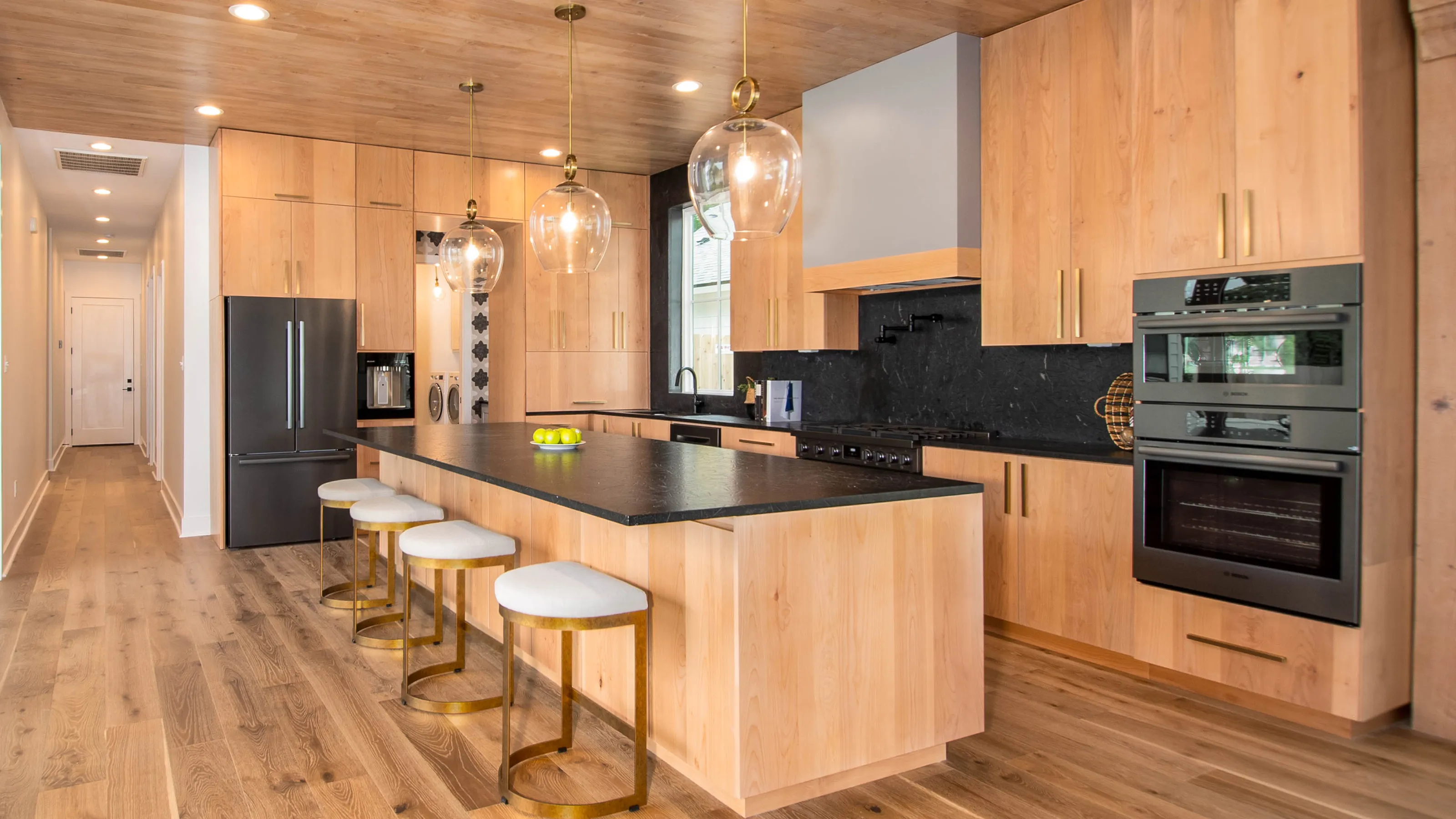 Modern kitchen with wood cabinets, island, pendant lights, and Bosch stainless steel appliances.