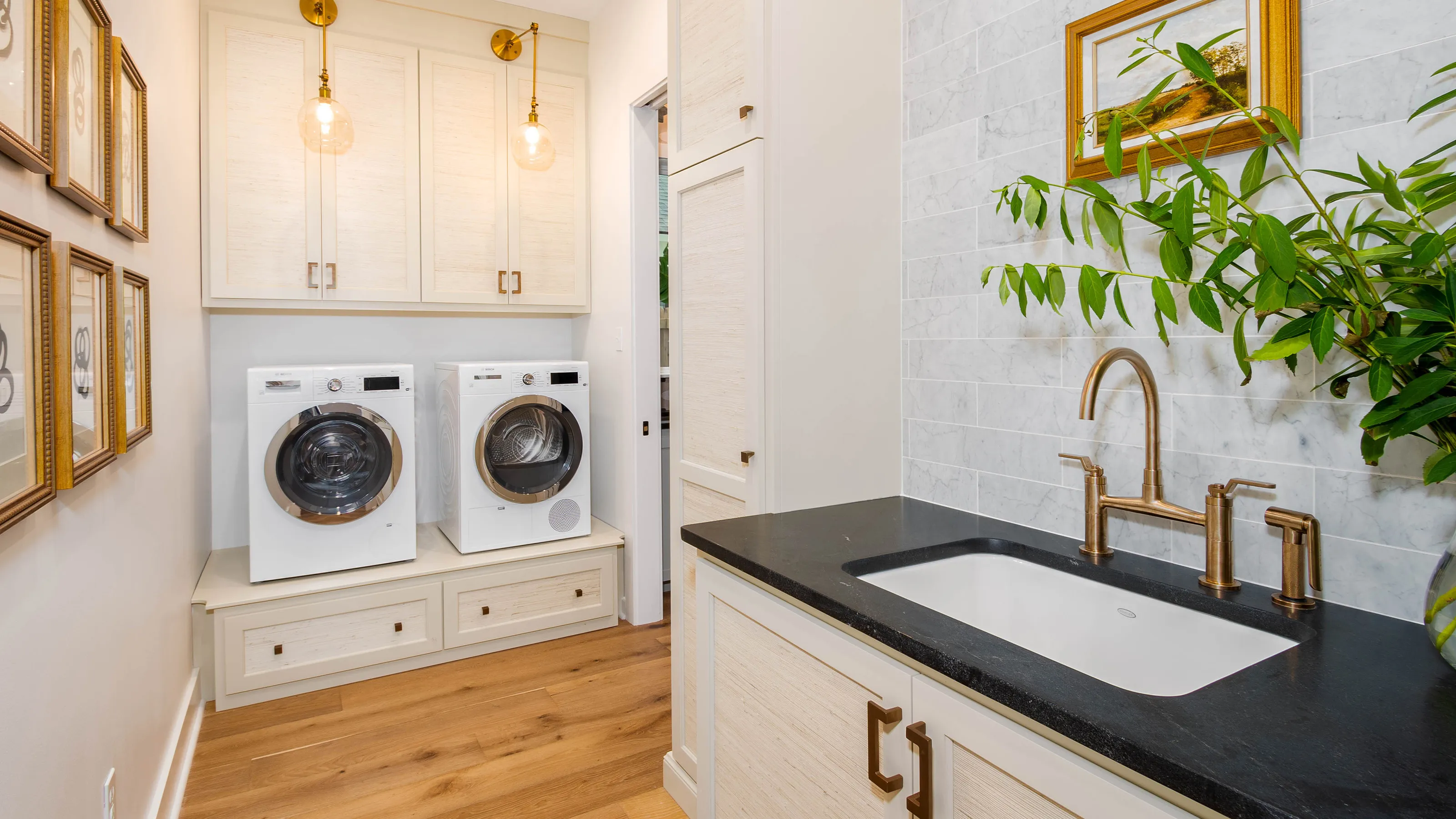 Laundry room with a Bosch washer, dryer, white cabinets, dark countertop, and decorative plants.