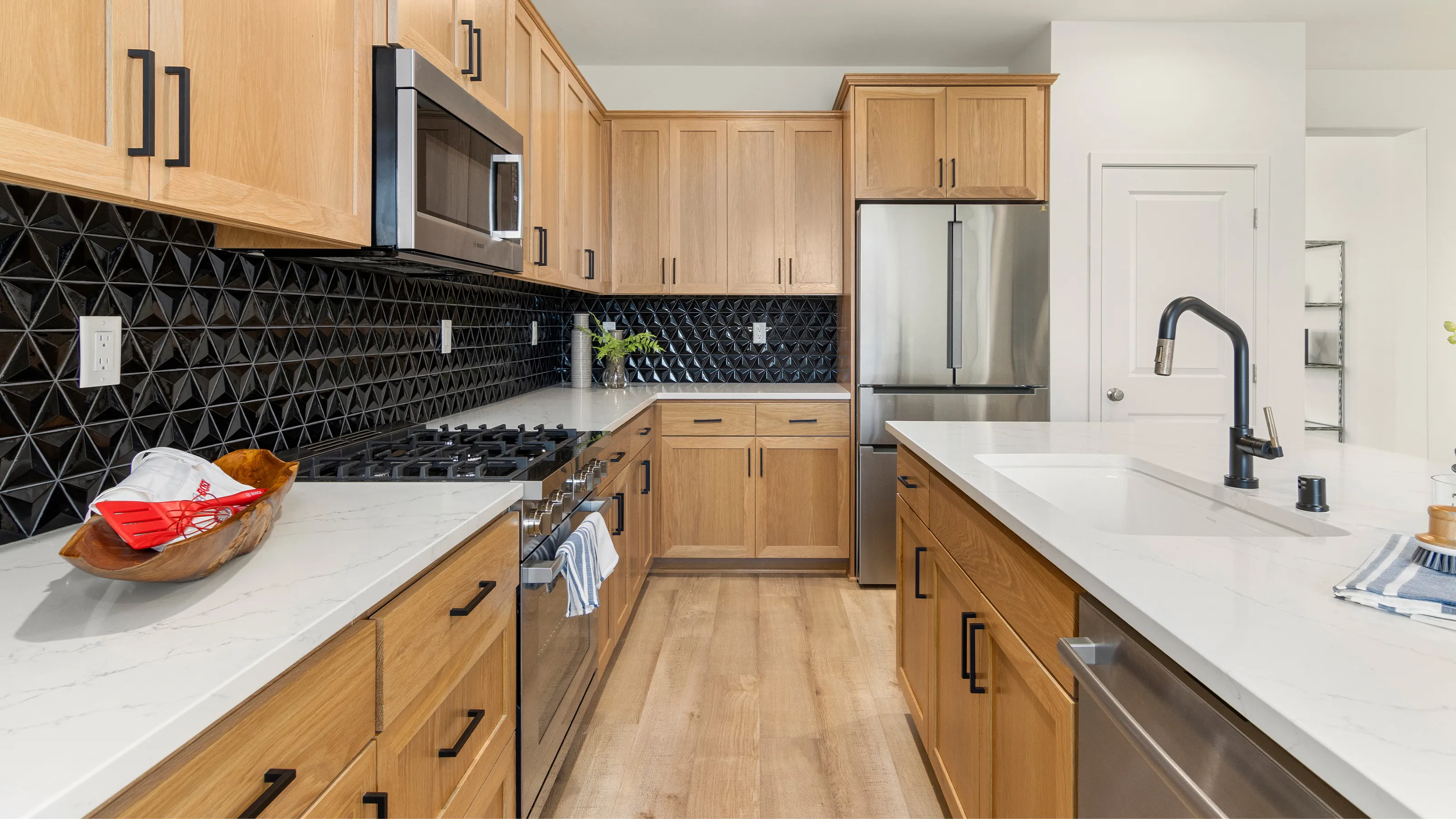 Modern kitchen with wooden cabinets, Bosch stainless steel appliances, and black tile backsplash.