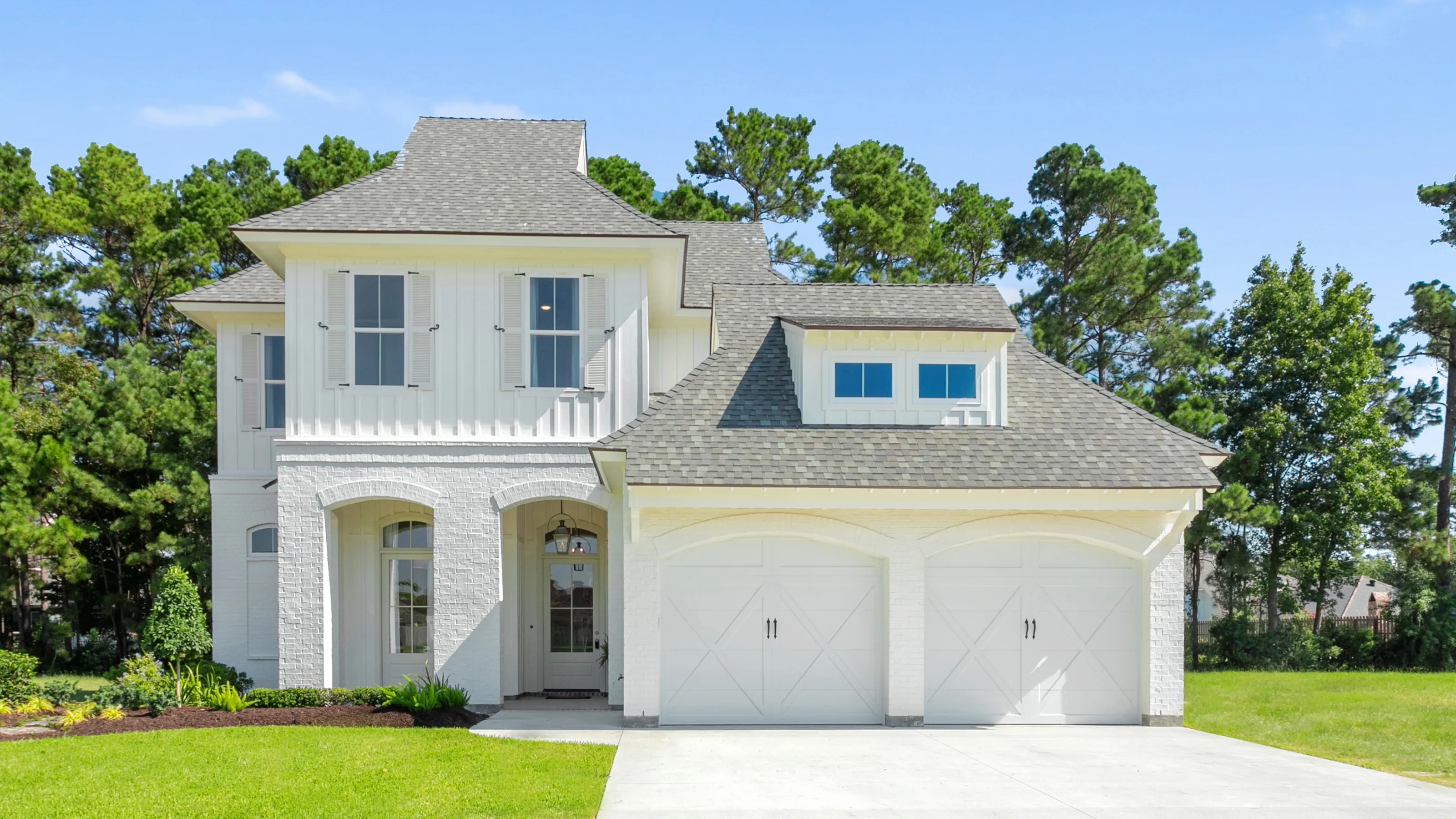 Two-story white house with two garage doors and a well-maintained lawn.